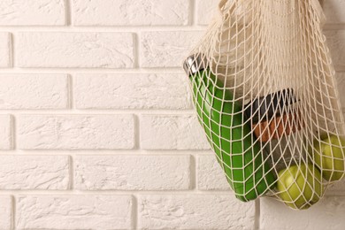 Photo of Net bag with different items hanging on brick wall, space for text. Conscious consumption