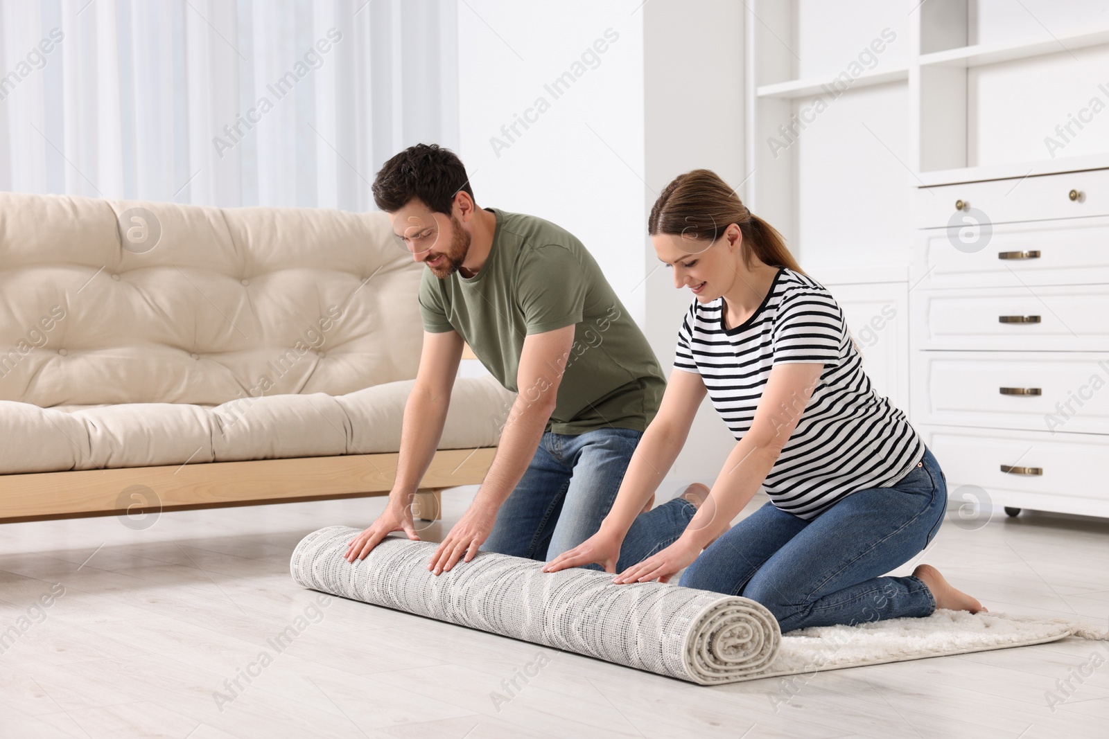 Photo of Smiling couple unrolling carpet with beautiful pattern on floor in room