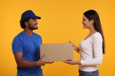 Smiling courier giving parcel to receiver on orange background