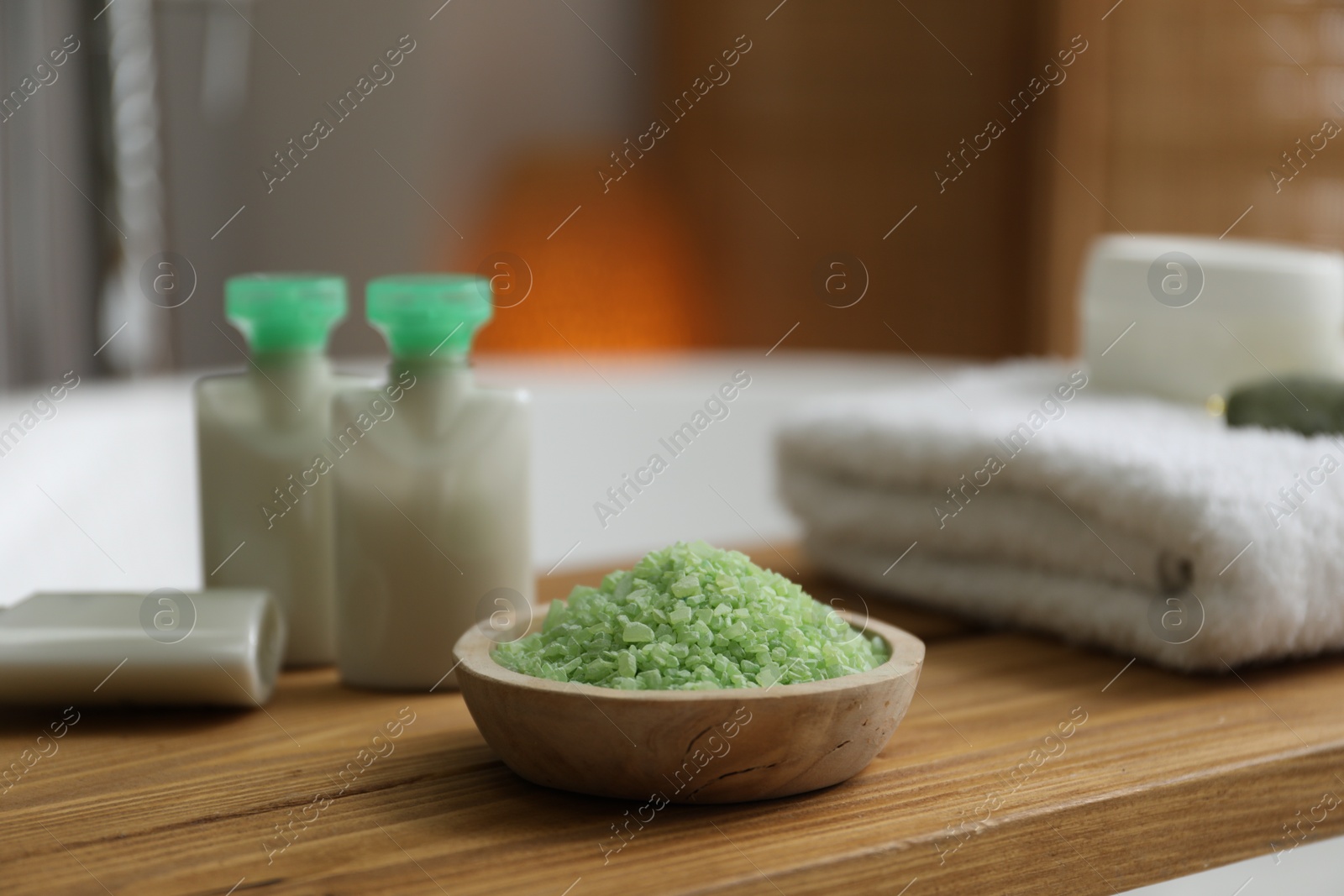 Photo of Wooden tray with cosmetic products, sea salt and towel on bath tub in bathroom, closeup
