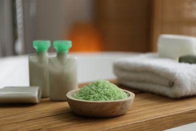 Wooden tray with cosmetic products, sea salt and towel on bath tub in bathroom, closeup