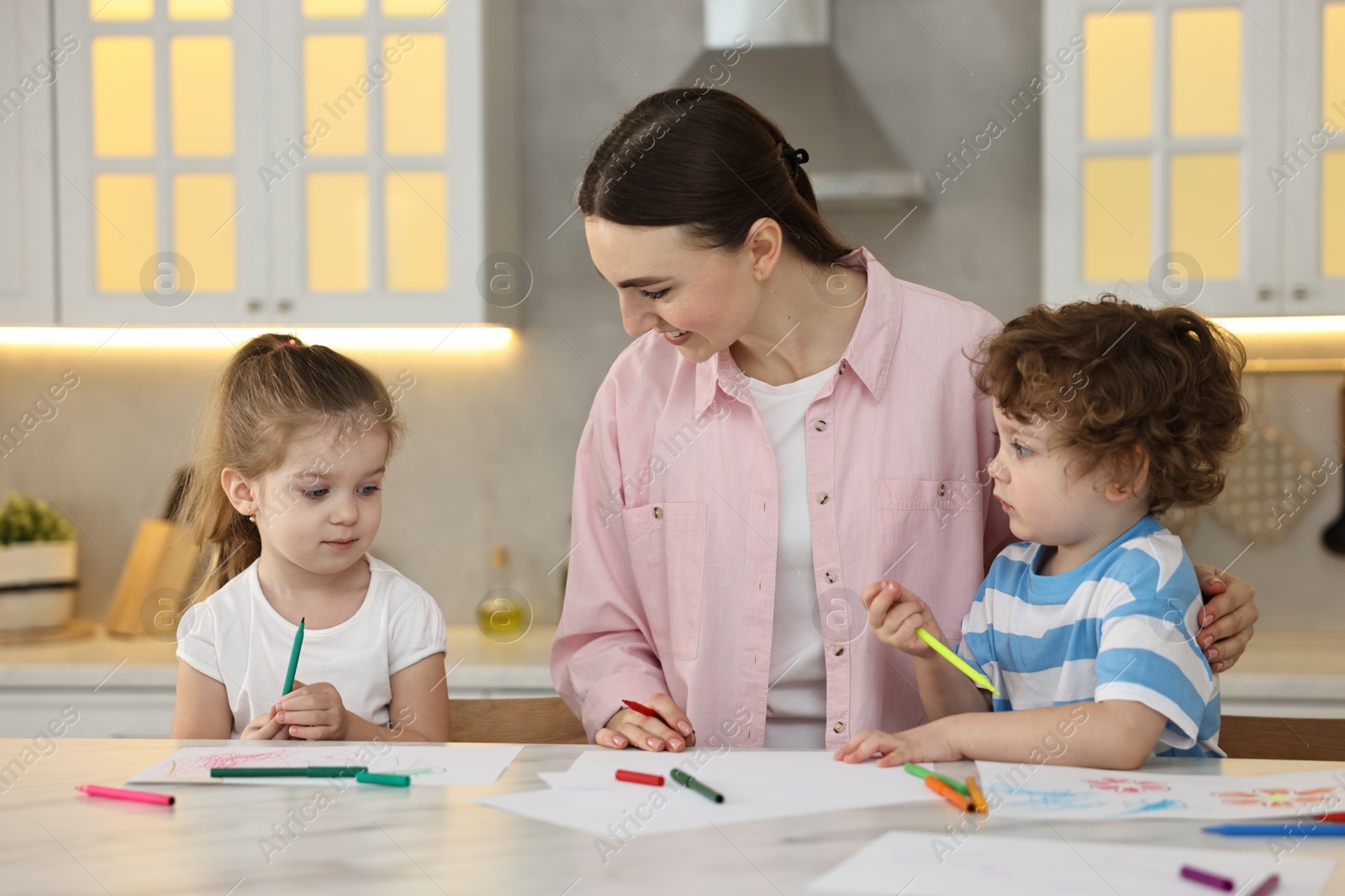 Photo of Mother and her little children drawing with colorful markers at table in kitchen