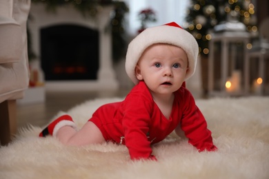 Photo of Cute little baby in red bodysuit and Santa hat on floor at home. Christmas suit