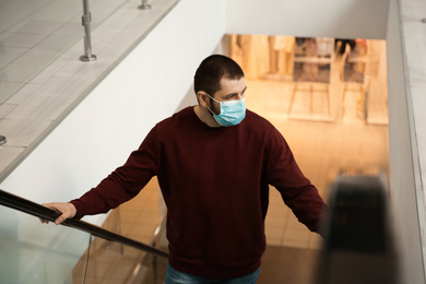 Photo of Man with disposable mask on escalator in mall. Dangerous virus