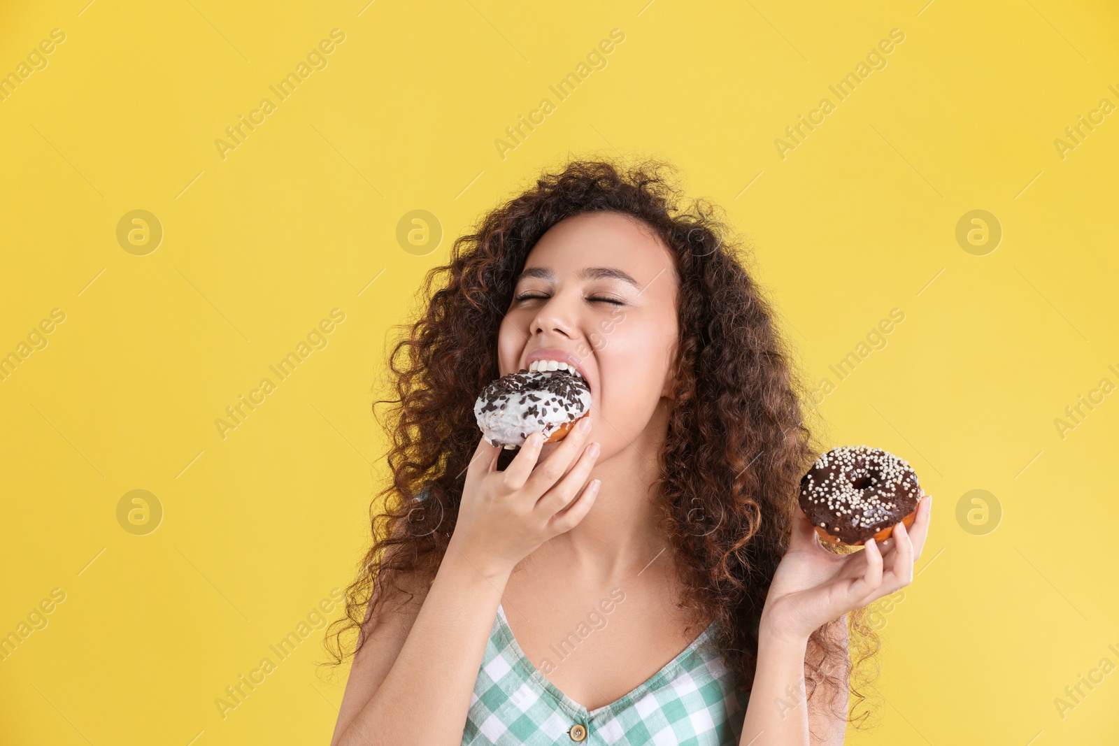 Photo of Beautiful African-American woman with donuts on yellow background