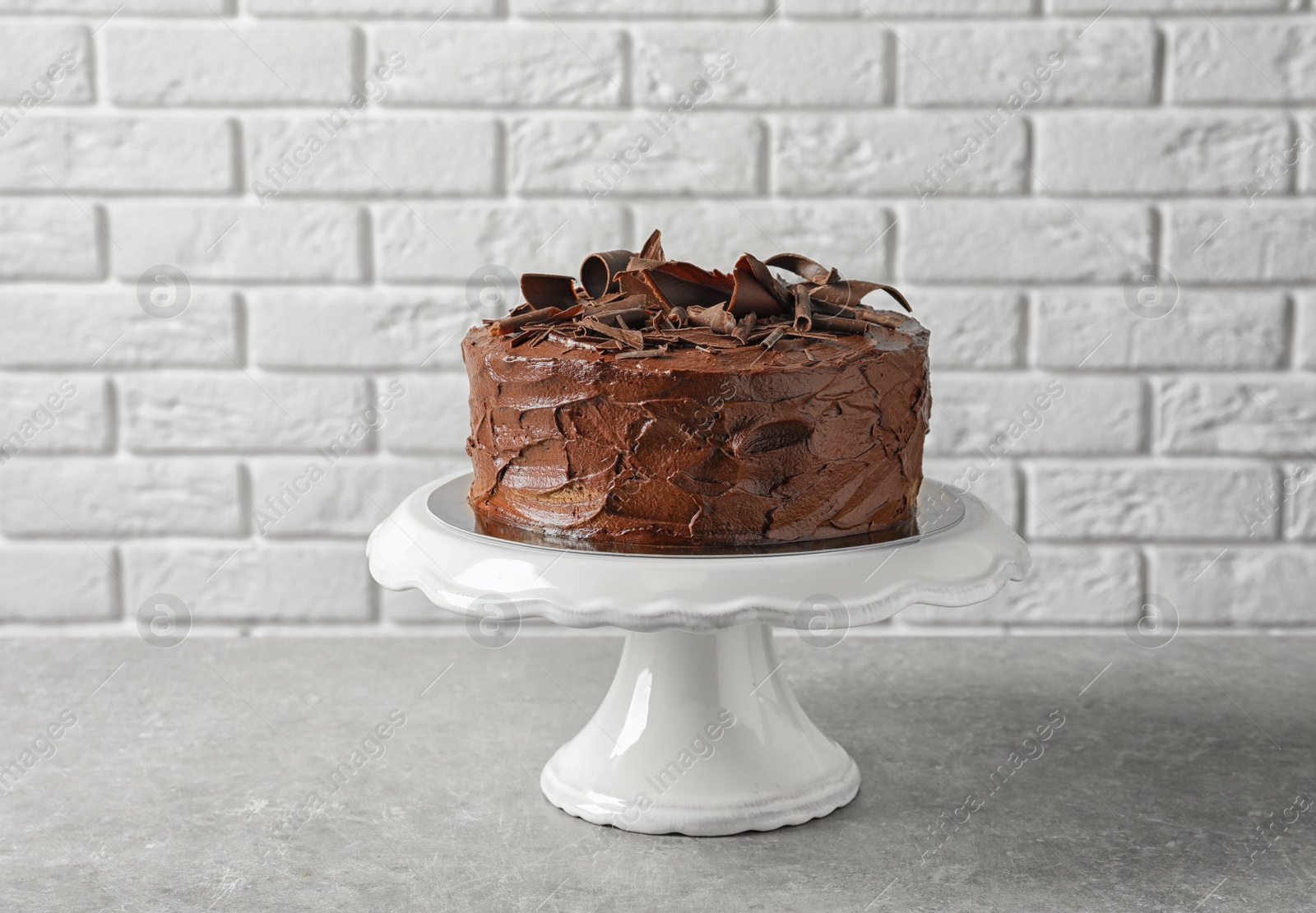 Photo of Stand with tasty homemade chocolate cake on table near brick wall