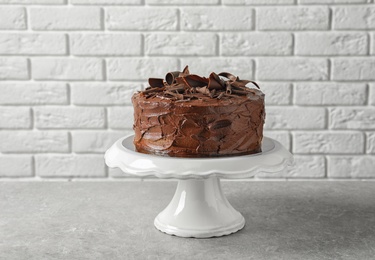 Stand with tasty homemade chocolate cake on table near brick wall