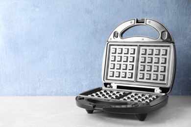 Photo of Modern waffle iron on grey marble table against light blue background. Space for text