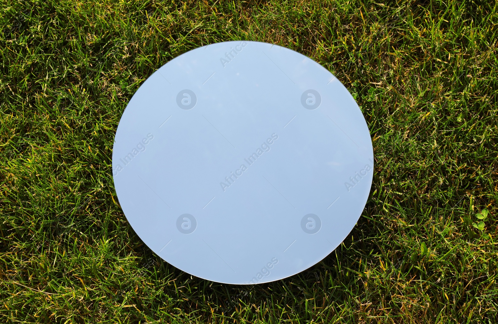 Photo of Spring atmosphere. Round mirror on grass reflecting sky, above view