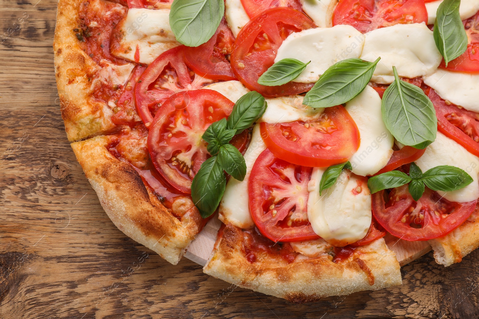 Photo of Delicious Caprese pizza with tomatoes, mozzarella and basil on wooden table, top view