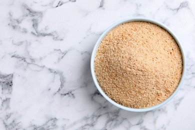 Fresh breadcrumbs in bowl on white marble table, top view. Space for text