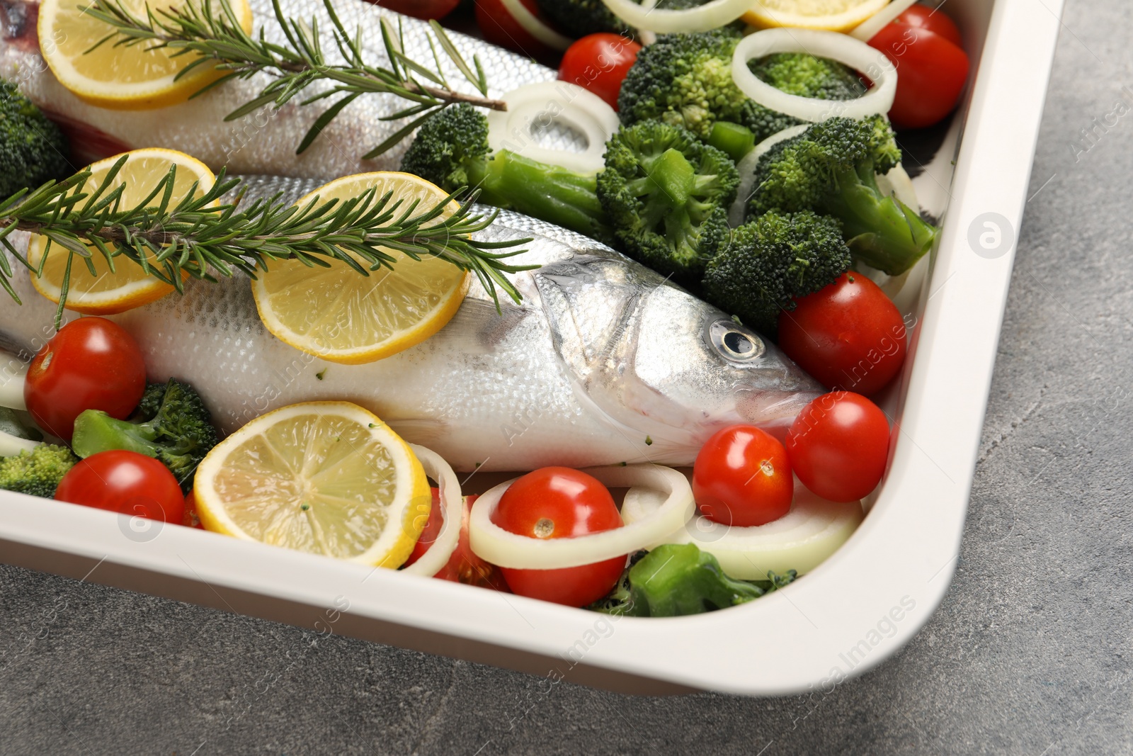 Photo of Raw fish with vegetables and lemon in baking dish on grey textured table