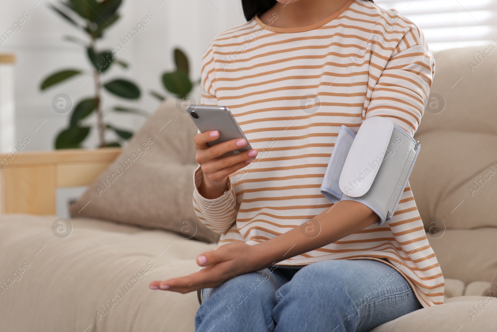 Photo of Woman checking blood pressure with modern monitor and smartphone indoors, closeup