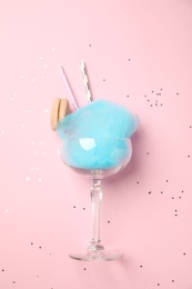 Photo of Glass with cotton candy and macaroon on pink background, top view