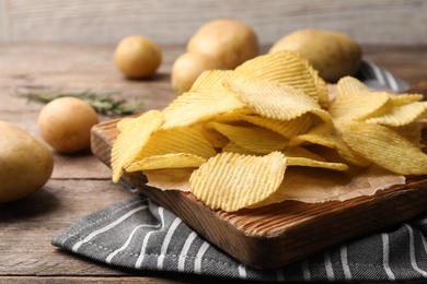 Board with crispy potato chips on wooden table