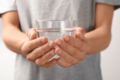 Photo of Man holding glass with fresh water against gray background, closeup