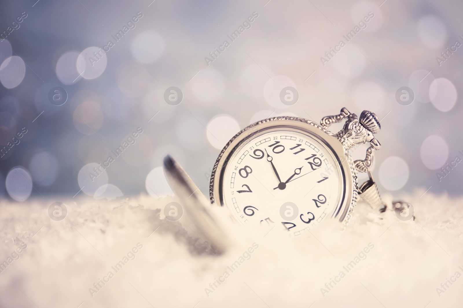 Photo of Pocket watch on snow against blurred lights, space for text. New Year countdown