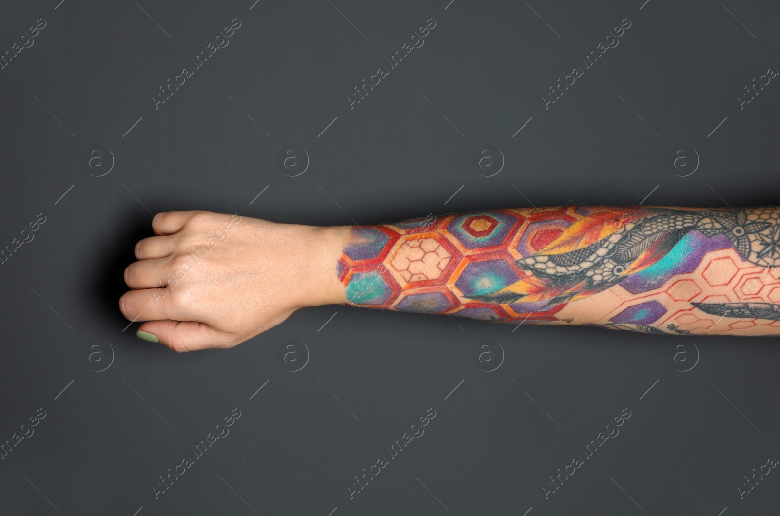 Photo of Woman with colorful tattoos on arm against dark grey background, closeup