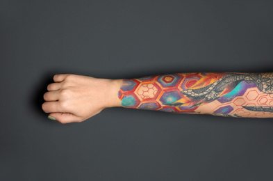 Woman with colorful tattoos on arm against dark grey background, closeup