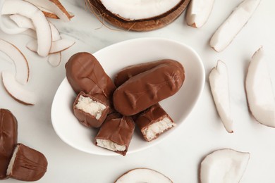 Photo of Delicious milk chocolate candy bars with coconut filling on white marble table, flat lay