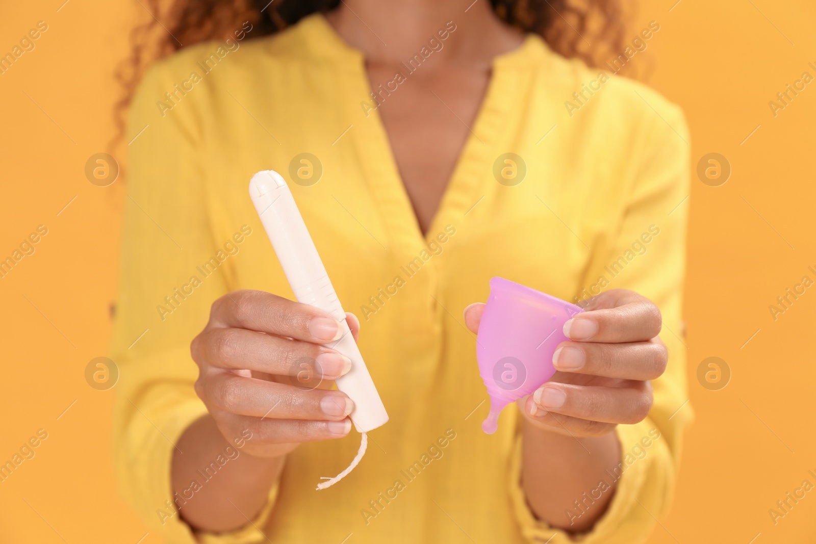 Photo of Young African American woman with tampon and menstrual cup on yellow background, closeup