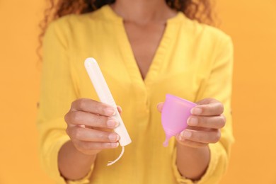 Young African American woman with tampon and menstrual cup on yellow background, closeup