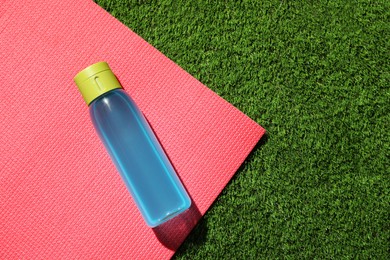 Bottle of light blue drink and mat on green grass, flat lay. Space for text