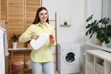 Photo of Beautiful young woman pouring detergent into cap in laundry room