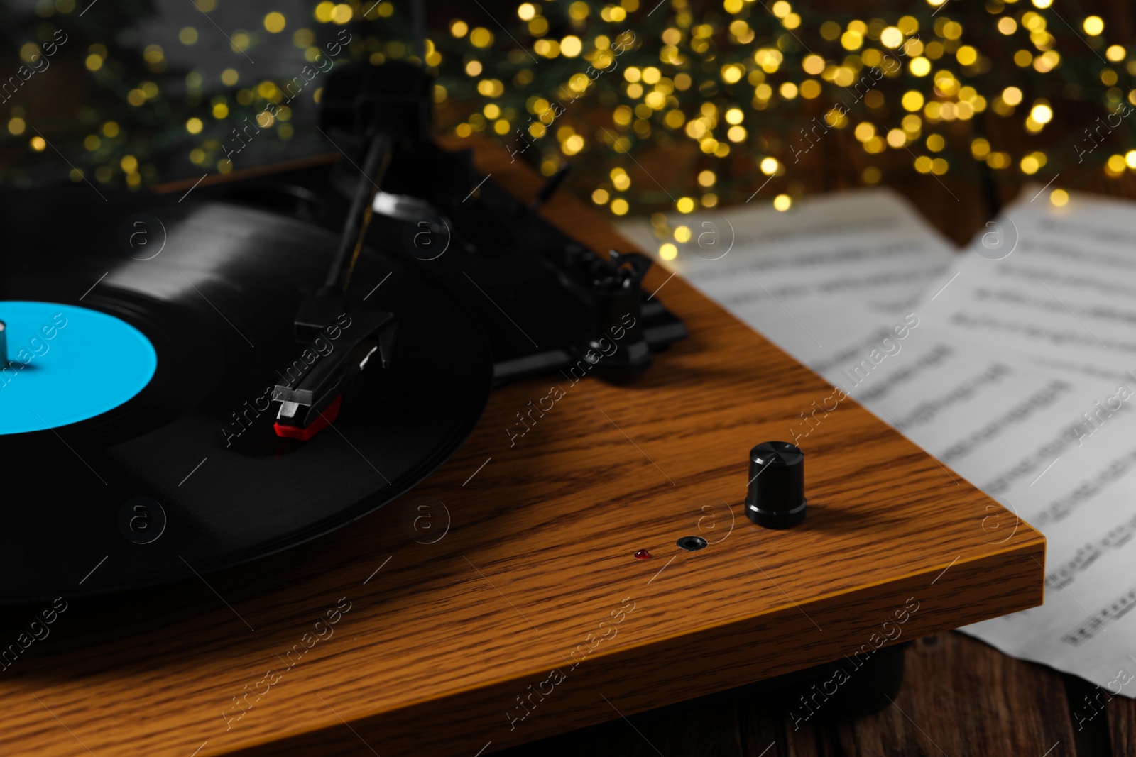 Photo of Closeup view of turntable with vinyl record and note sheets on wooden table against blurred lights