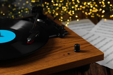 Photo of Closeup view of turntable with vinyl record and note sheets on wooden table against blurred lights