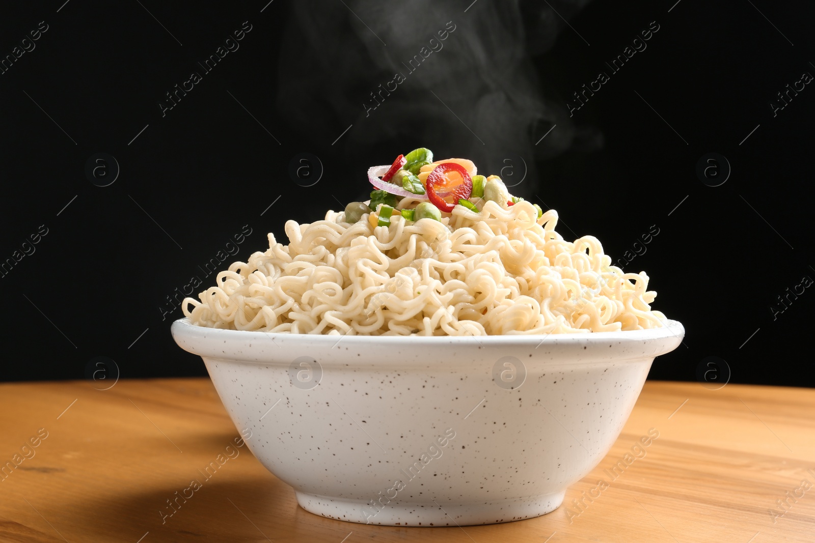 Photo of Bowl of hot noodles with vegetables on table against black background