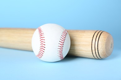 Photo of Wooden baseball bat and ball on light blue background, closeup. Sports equipment