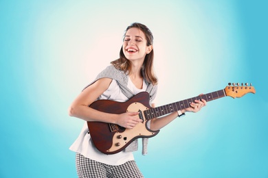 Young woman playing electric guitar on color background