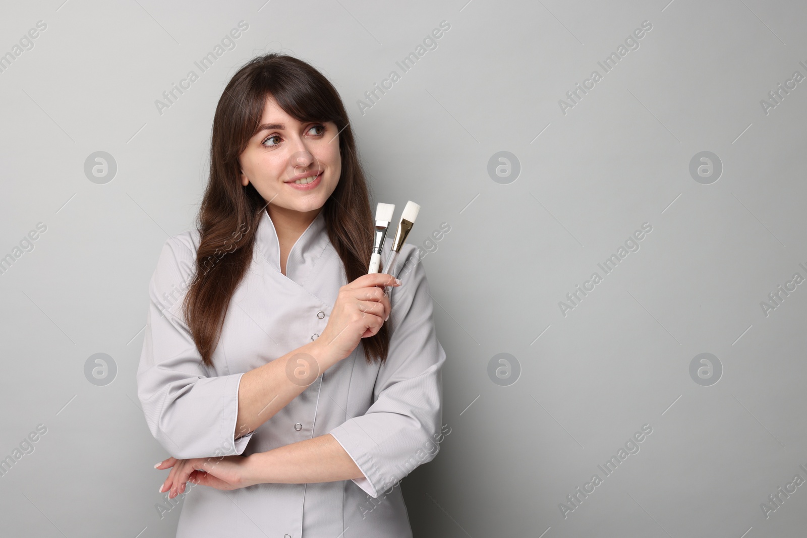 Photo of Cosmetologist with cosmetic brushes on grey background, space for text