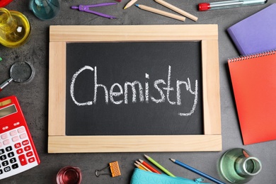 Laboratory glassware, school supplies and board with word CHEMISTRY on grey background, flat lay