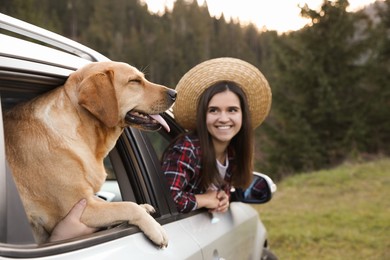Photo of Adorable dog and happy woman looking out of car window in mountains. Traveling with pet