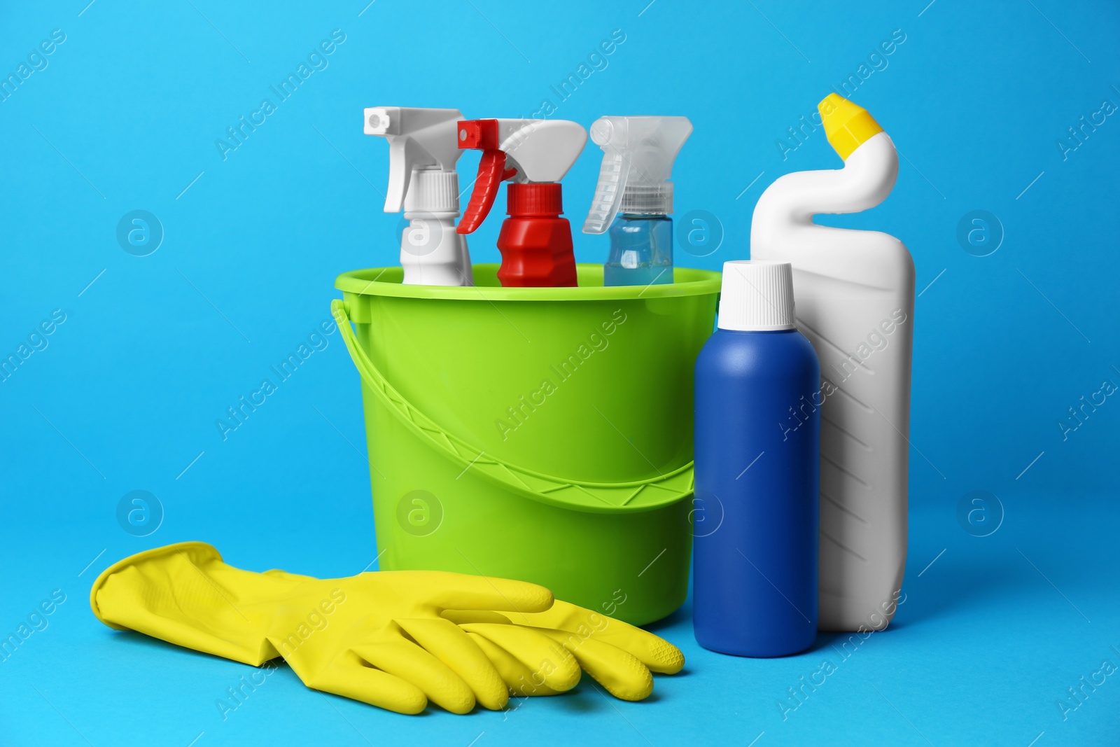 Photo of Green bucket, cleaning supplies and tools on light blue background