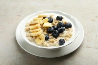 Tasty oatmeal with banana, blueberries, butter and milk served in bowl on light grey table