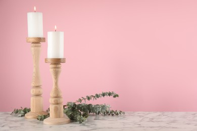Photo of Elegant candlesticks with burning candles and eucalyptus on white marble table. Space for text