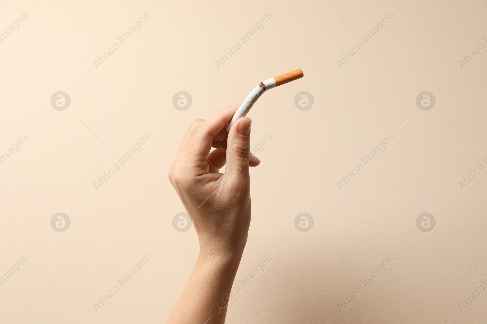 Photo of Stop smoking. Woman holding broken cigarette on beige background, closeup