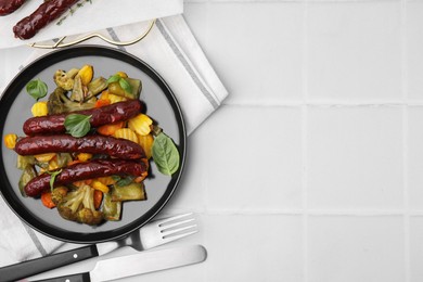Photo of Delicious smoked sausages and baked vegetables served on white tiled table, flat lay. Space for text