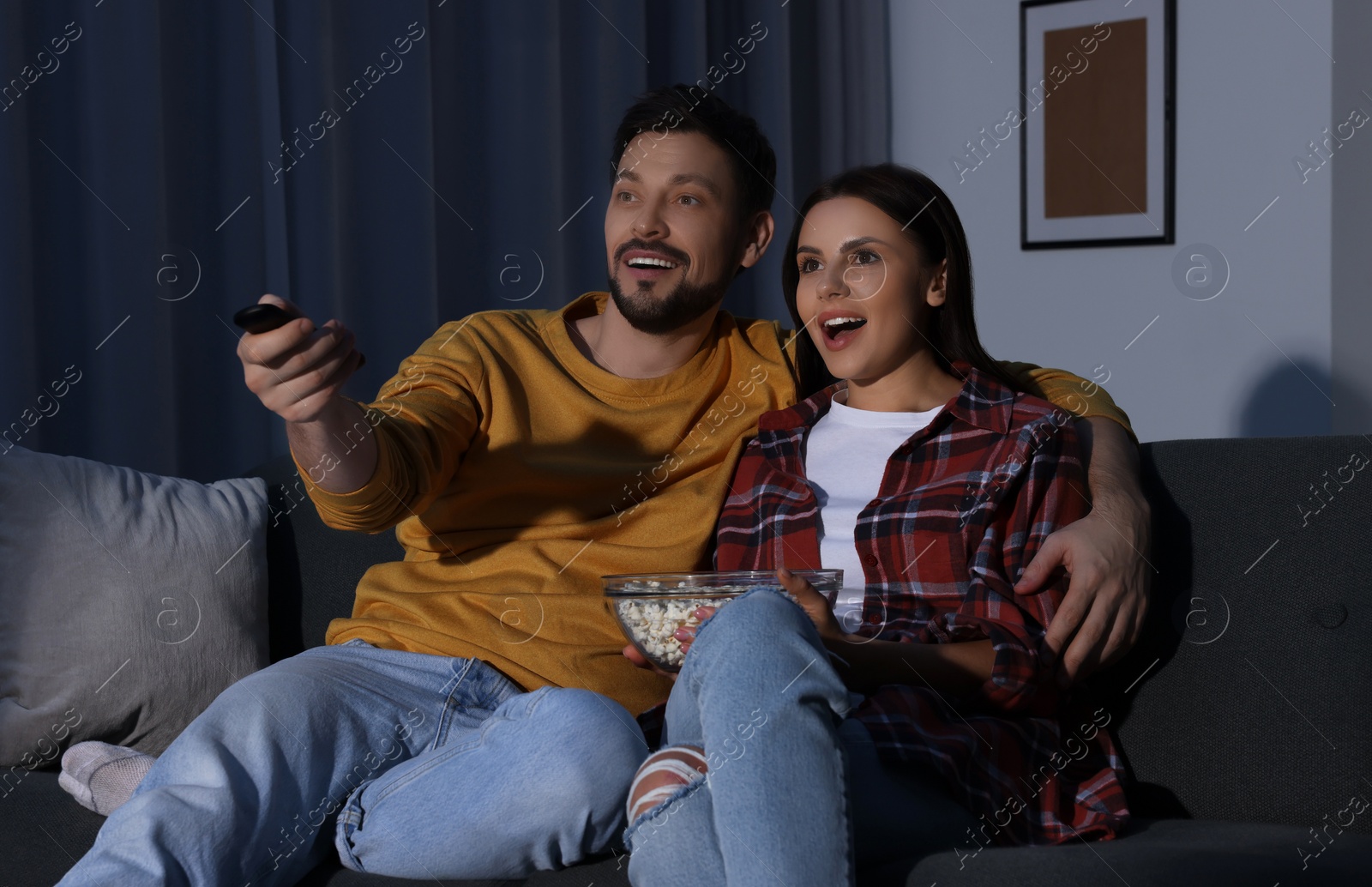 Photo of Couple watching TV at home in evening. Man changing channels with remote control