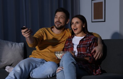 Couple watching TV at home in evening. Man changing channels with remote control