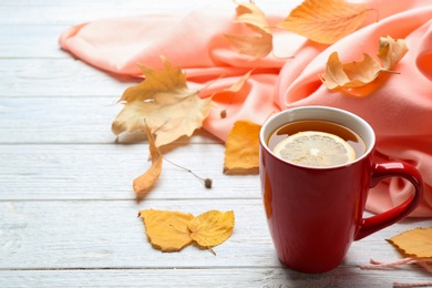 Photo of Cup of hot drink and leaves on white wooden table, space for text. Cozy autumn atmosphere