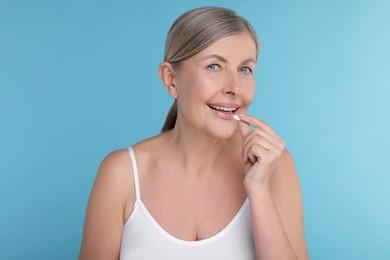 Beautiful woman taking vitamin pill on light blue background