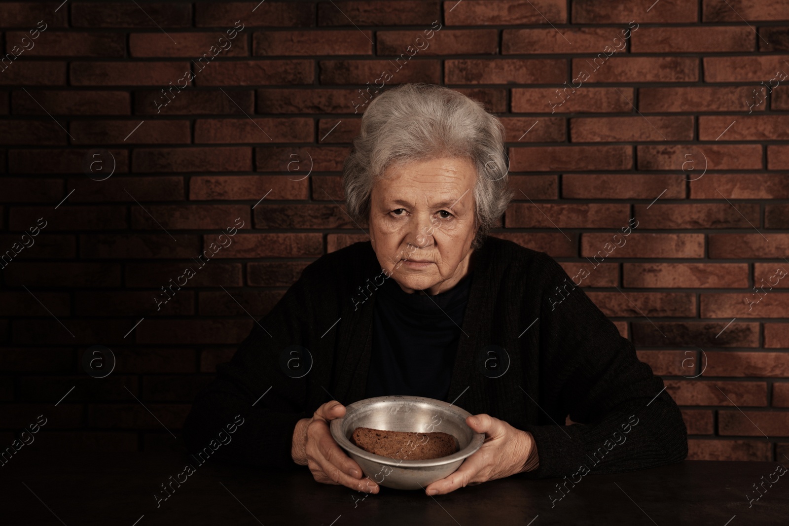 Photo of Poor mature woman with bread and bowl at table