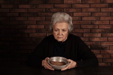 Poor mature woman with bread and bowl at table