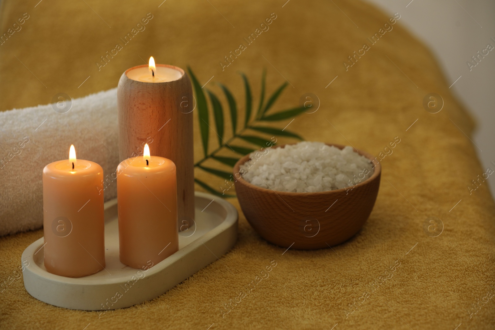 Photo of Spa composition. Burning candles, sea salt and towel on soft yellow surface