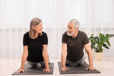 Photo of Senior couple practicing yoga on mats at home