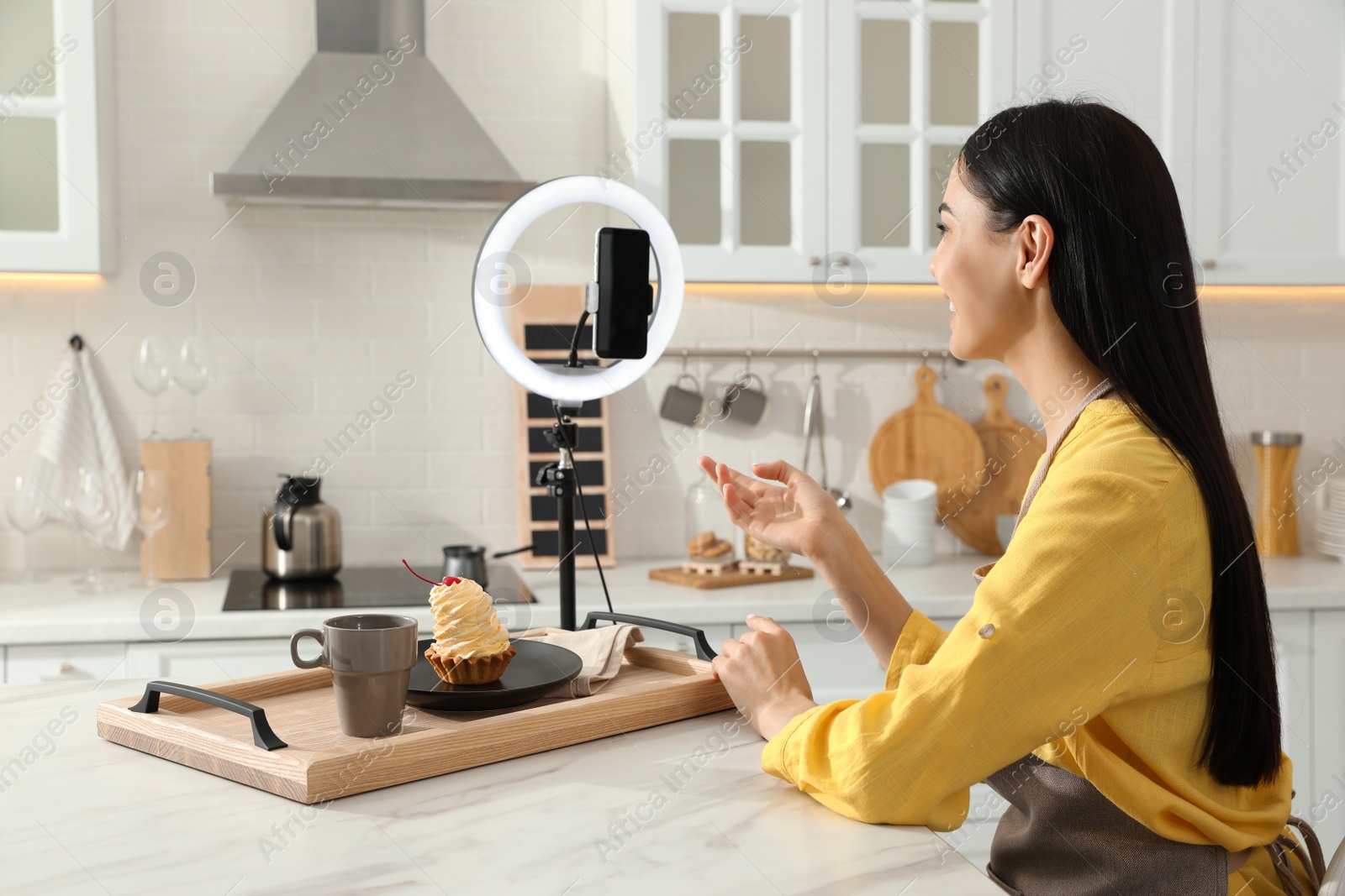 Photo of Blogger with tasty cake recording video in kitchen at home. Using ring lamp and smartphone